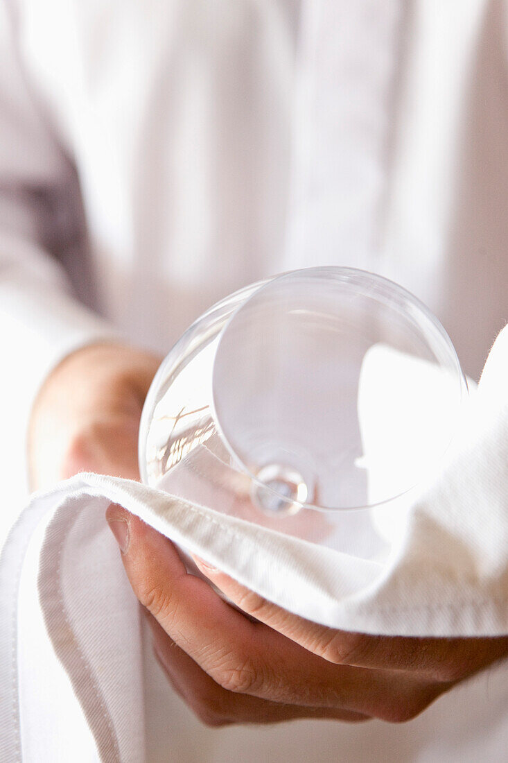 Close up of a waiter's hands polishing a wine glass with a napkin