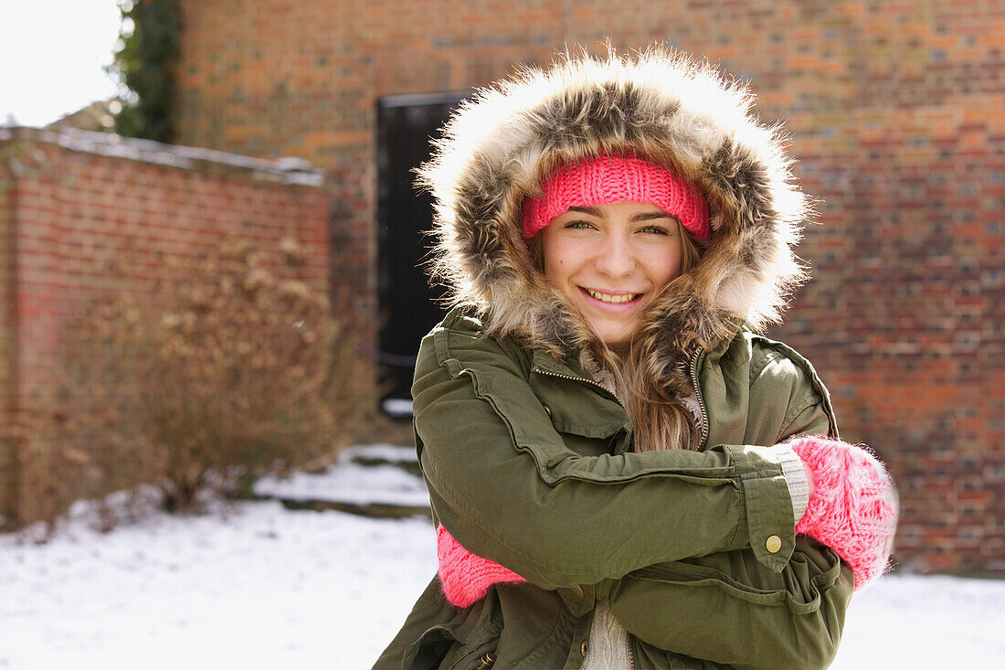 Smiling Teenage Girl Wearing Parka Hugging Herself Outdoors