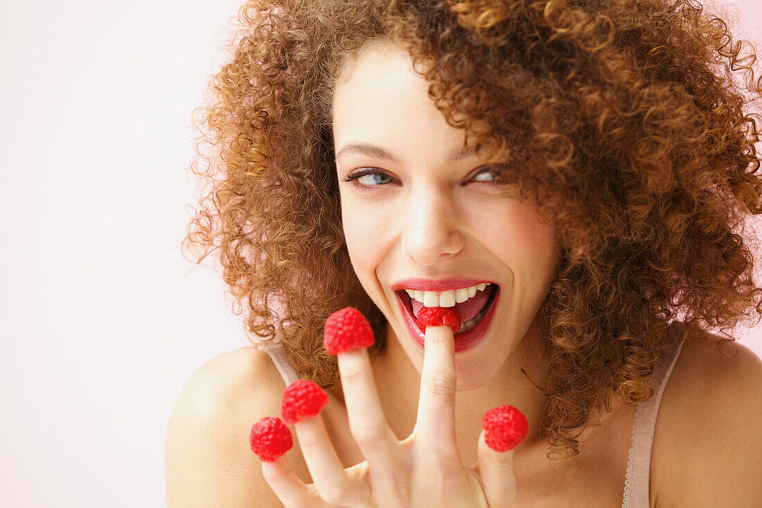 Smiling Young Woman Biting and Wearing Raspberries on Fingertips