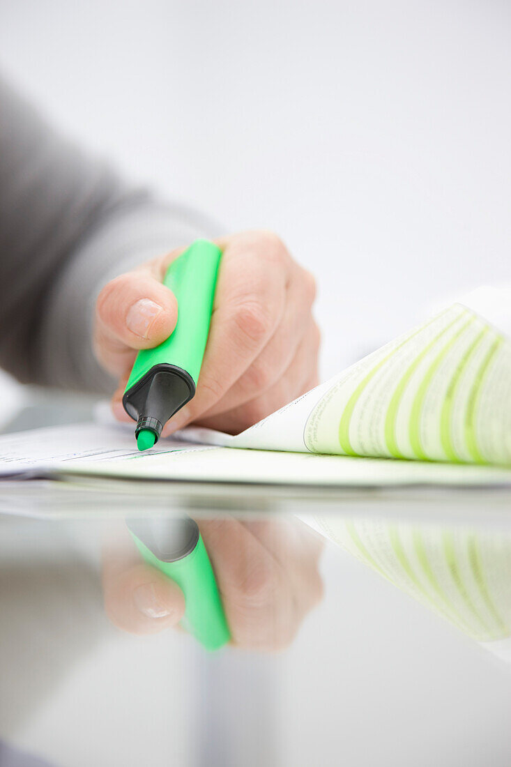 Close up of a woman hand holding a green highlighter over a paper document