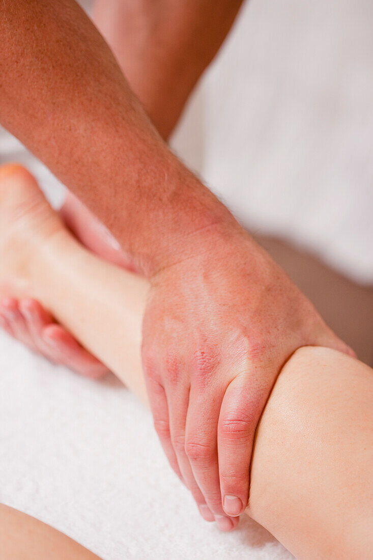 Extreme close up of a masseur hands massaging a woman leg