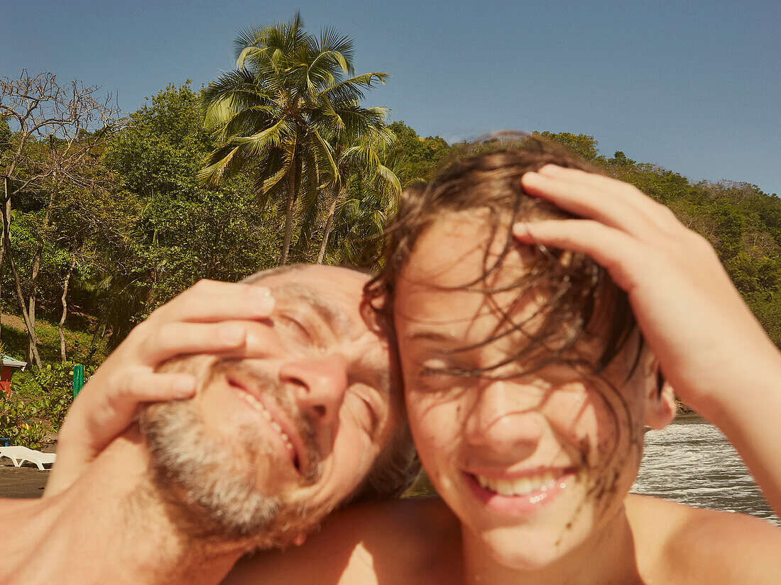 Portrait glücklicher Vater und Sohn lachend und umarmend am sonnigen Strand, St. Vincent und die Grenadinen