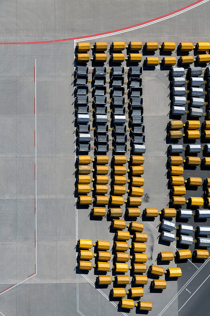 View from above empty yellow and black luggage carts on sunny airport tarmac