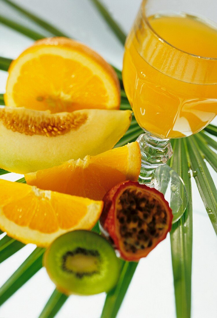 Ein Glas Orangensaft auf Palmenblatt und frische Früchte