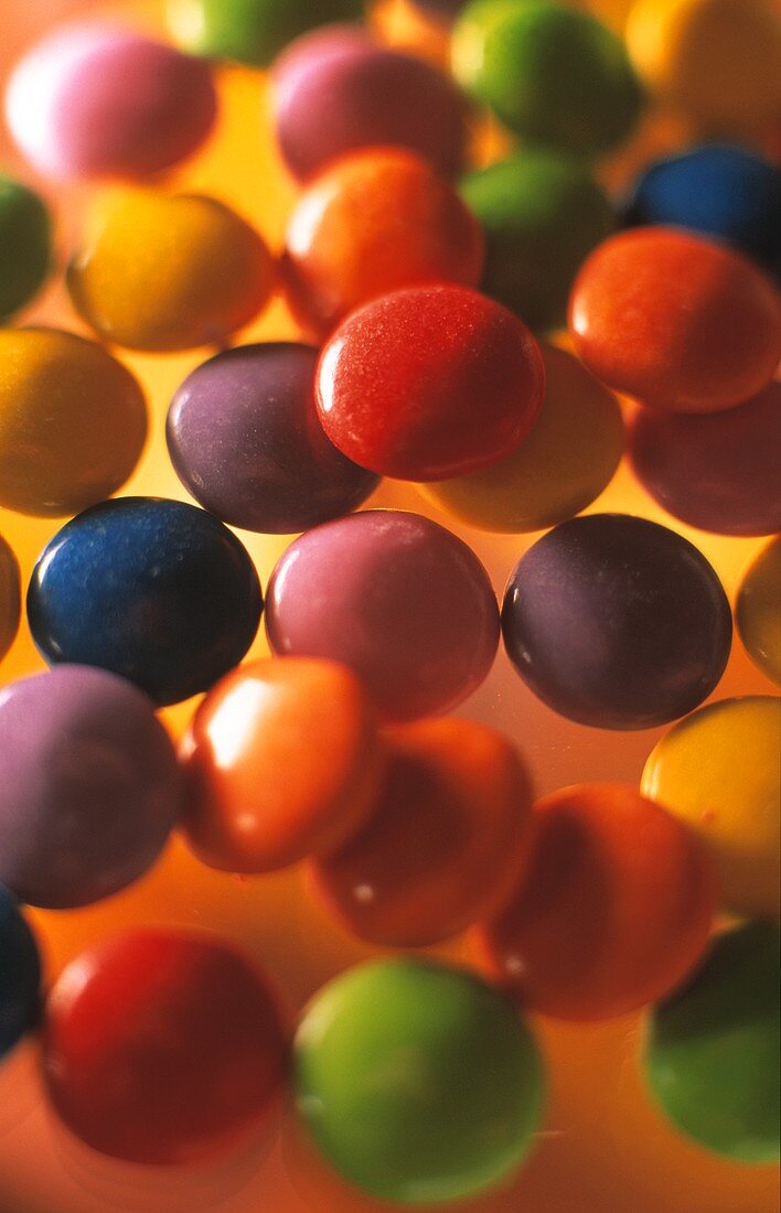 Colourful chocolate beans (Smarties) on yellow background