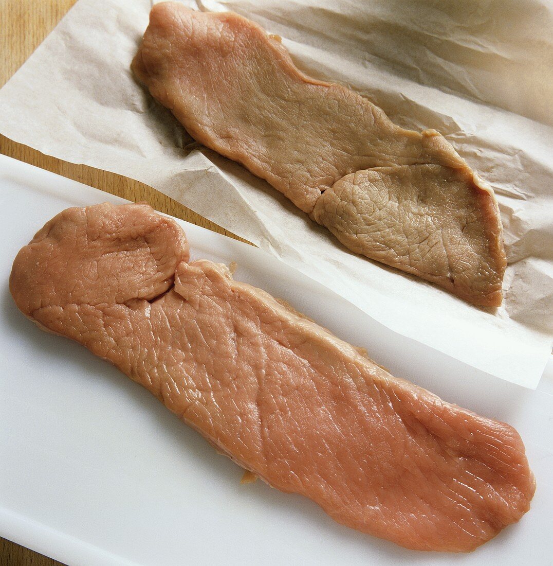 Veal escalopes; one on chopping board, one still on paper