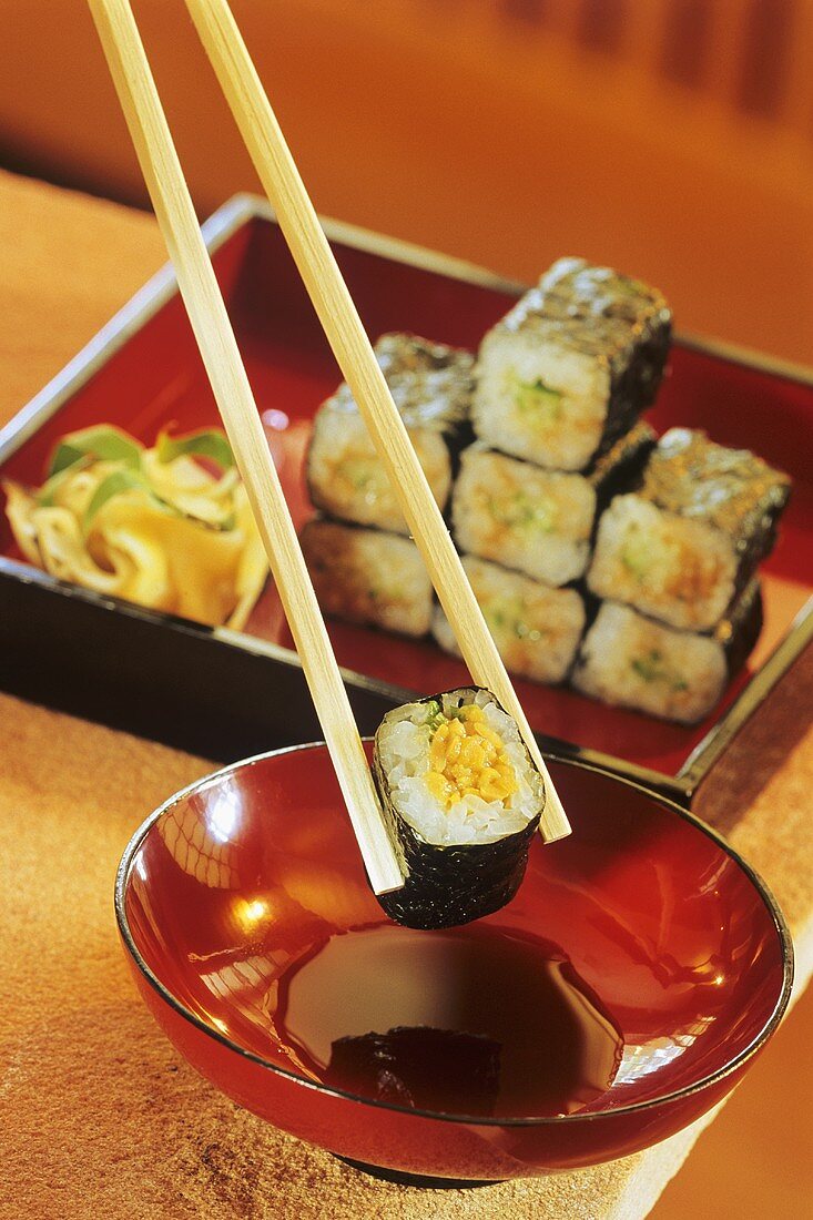 Chopstick with an umekyo natto maki above red bowl