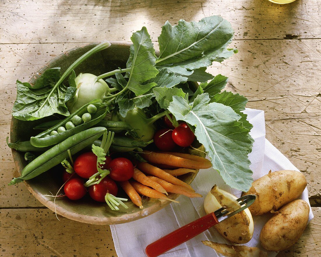 Spring vegetables in wooden bowl, potatoes with peeler