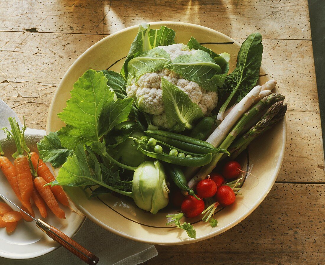 Various spring vegetables in a bowl, carrots beside it