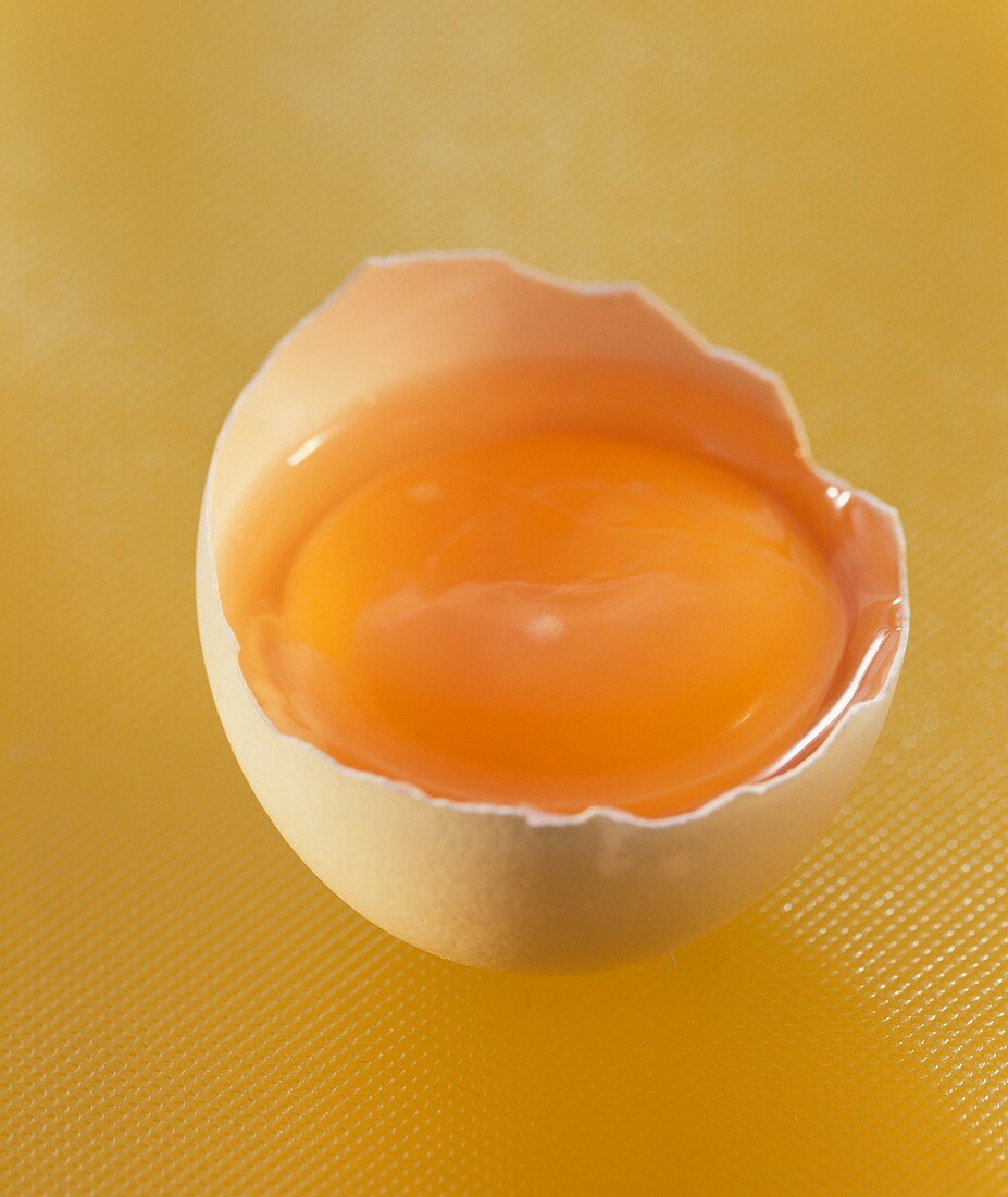 Aufgeschlagenes halbes Ei auf gelbem Untergrund