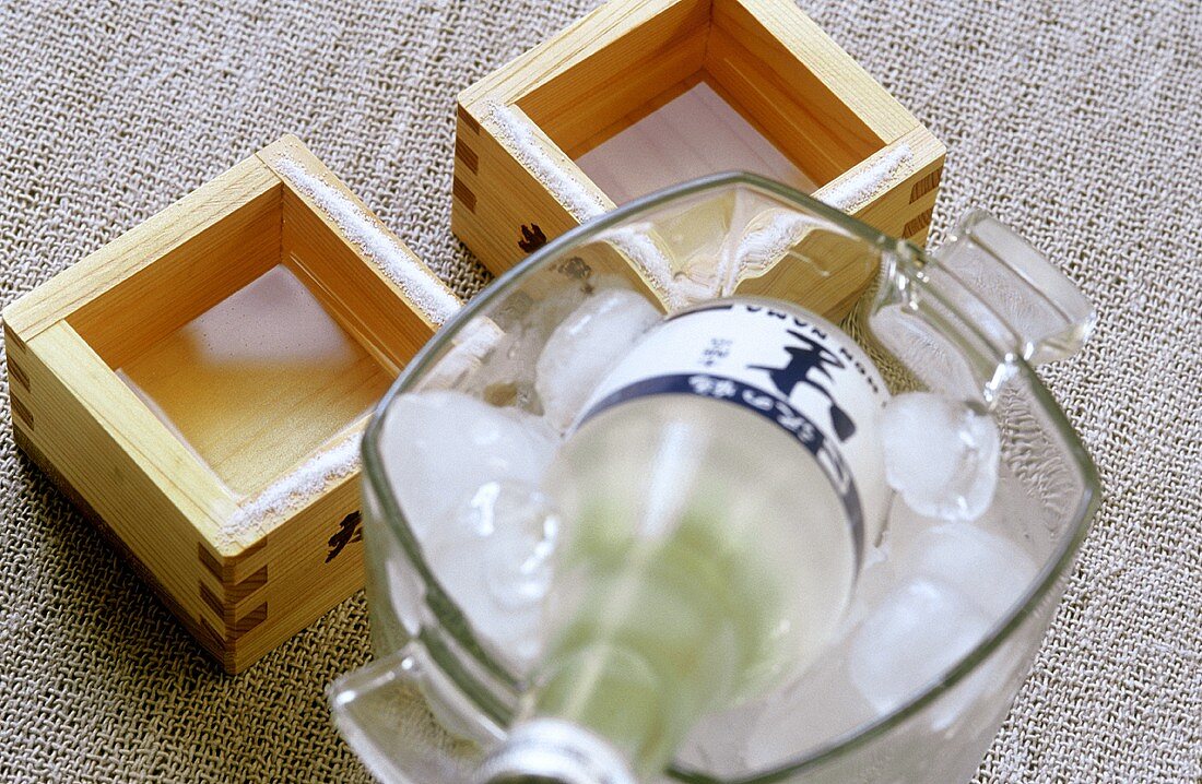 Flasche kalter Sake im Eiskübel und Sake in Holzschälchen