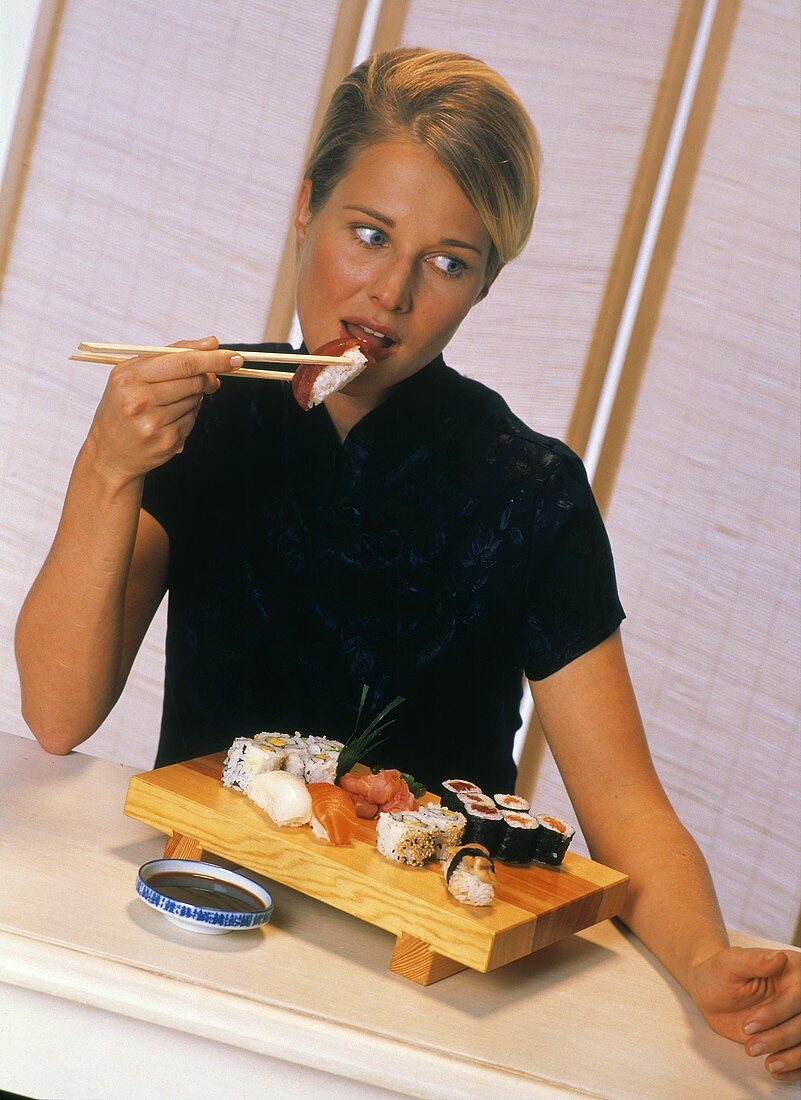 Young blond woman eating sushi with chopsticks