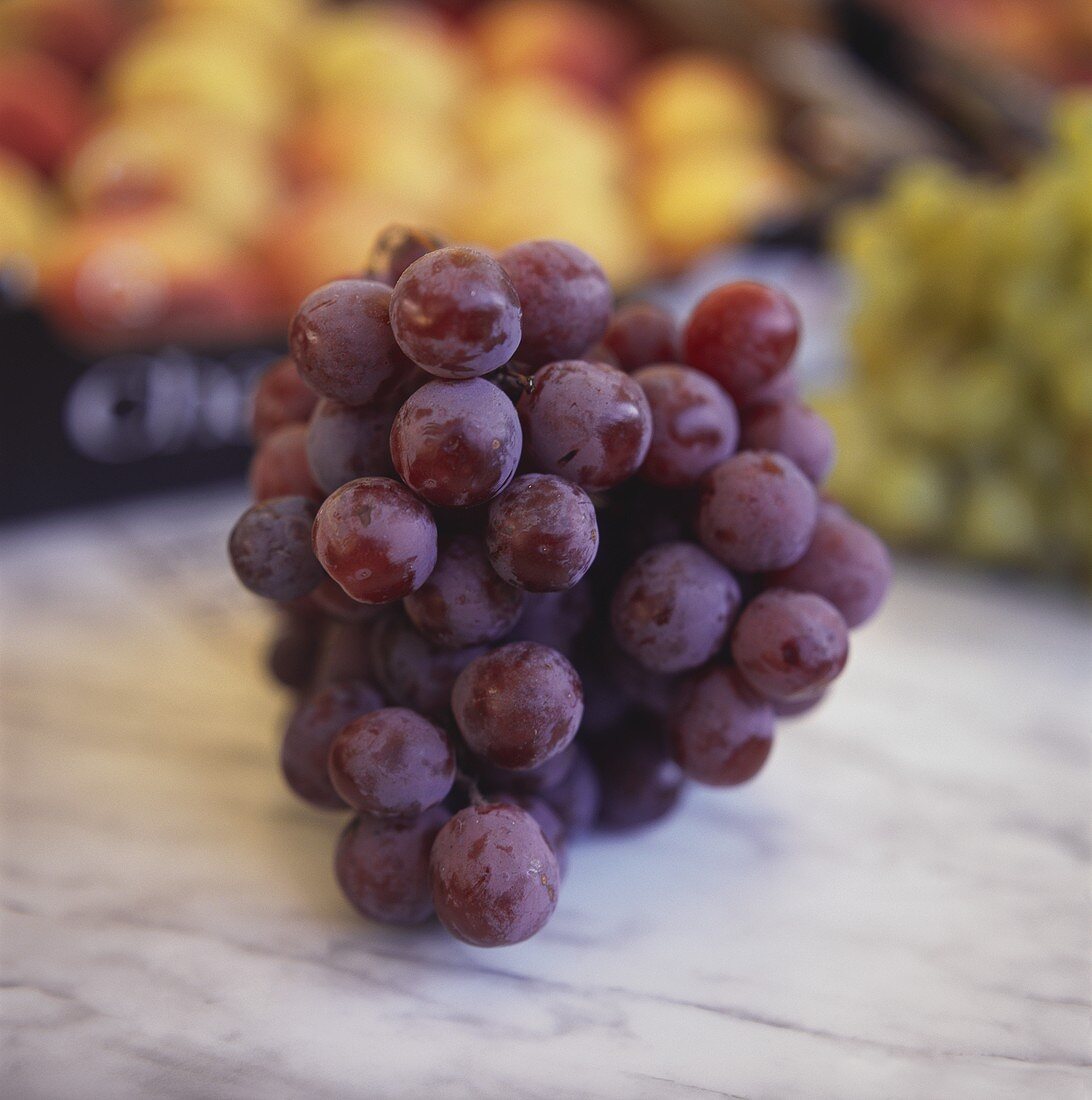 Red grapes on marble slab at market in front of other fruits