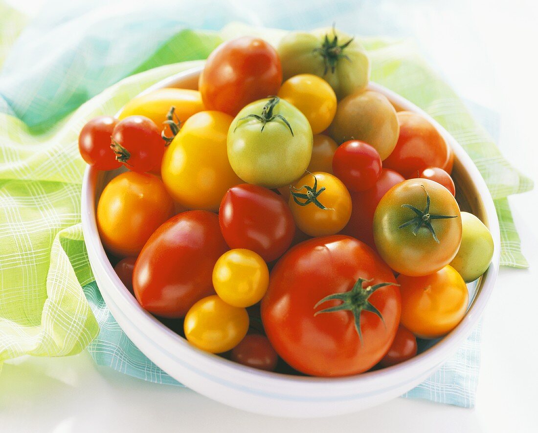 Various types of tomatoes in dish on green cloth