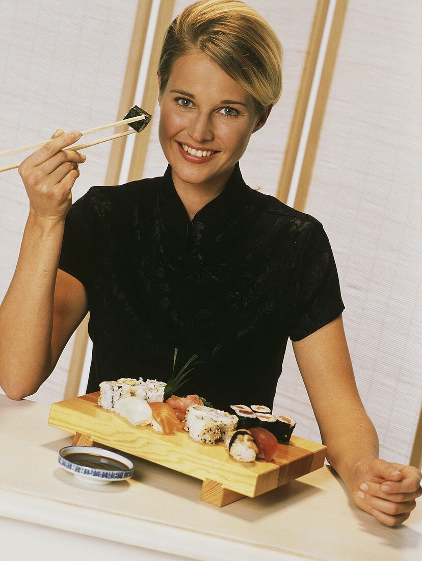 Junge blonde Frau hält ein Sushi mit Stäbchen