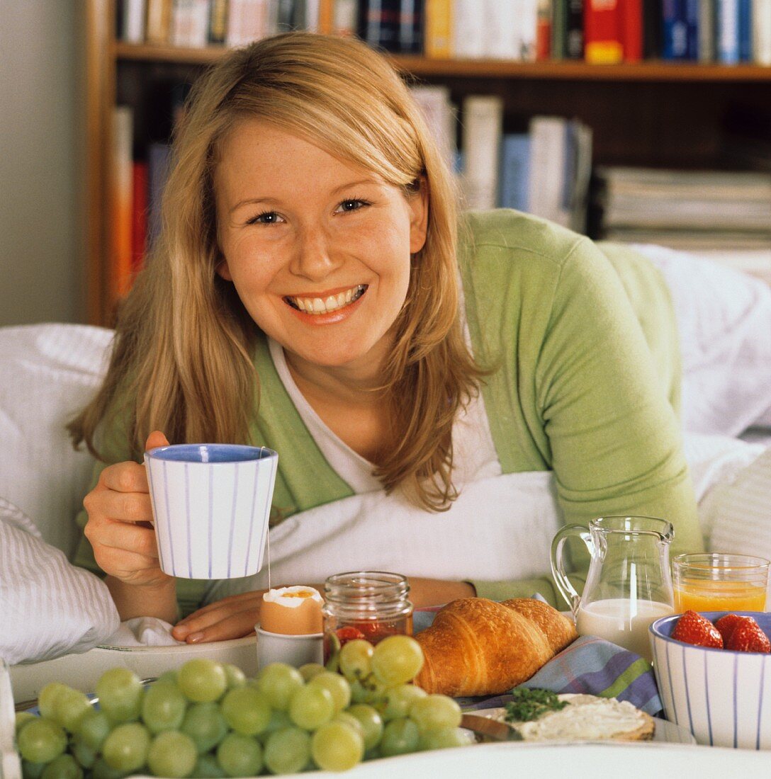 Junge Frau mit Frühstückstablett & Teetasse auf dem Bett