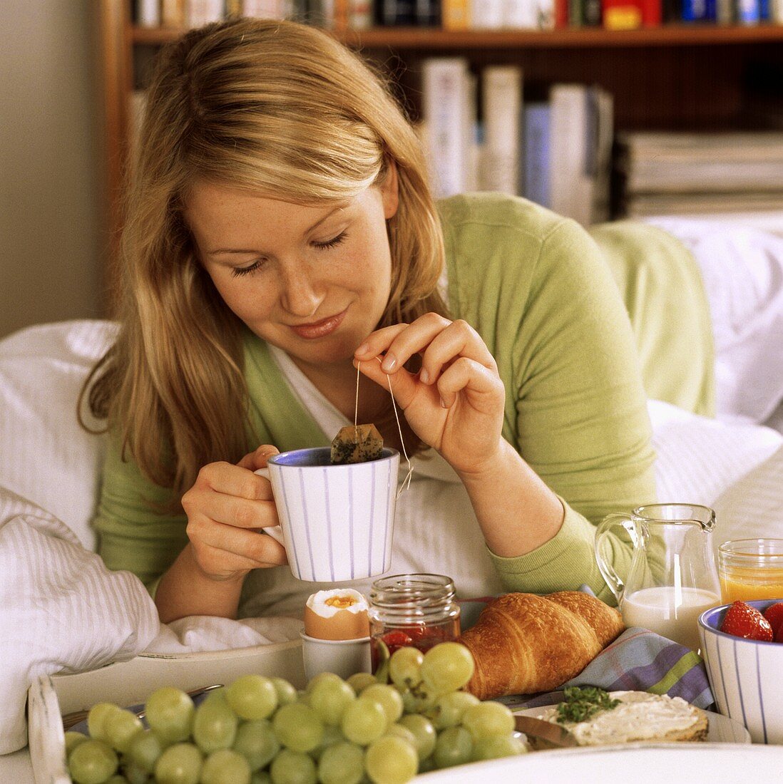 Young woman with breakfast tray and tea cup on bed