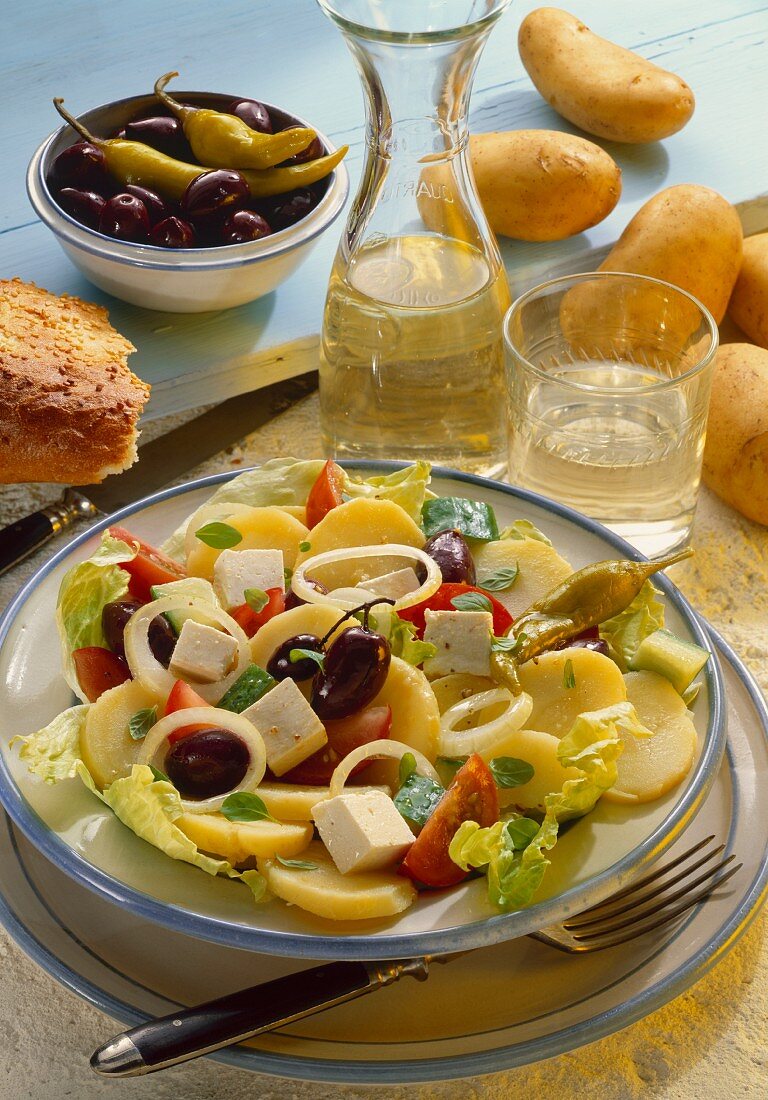 Griechischer Kartoffelsalat, daneben Wein, Brot, Oliven etc.