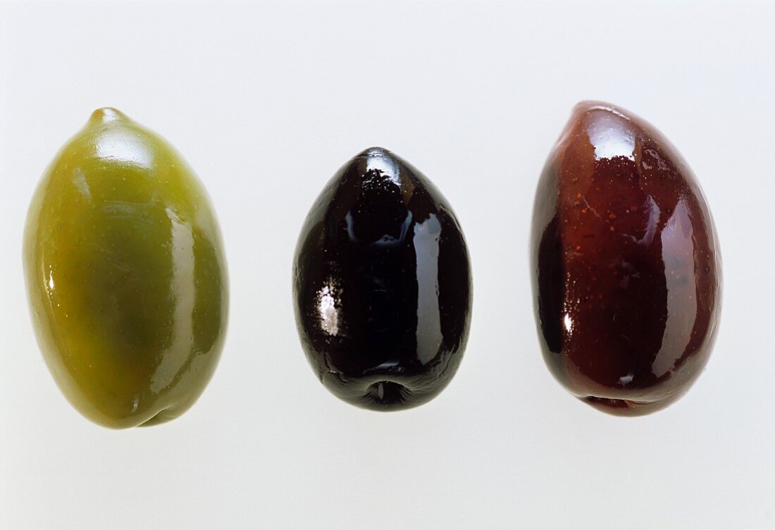 Drei verschiedenfarbige Oliven liegen in einer Reihe