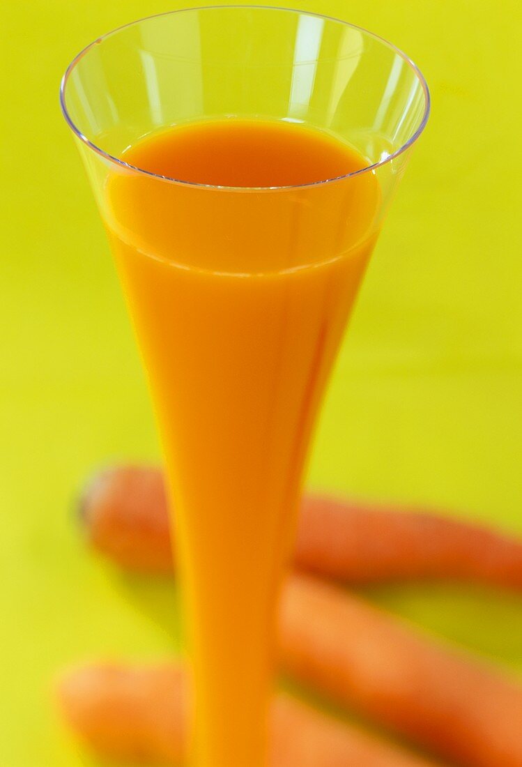 Ein Glas Karottensaft, daneben Möhren dekoriert
