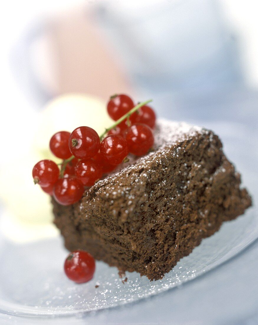 A piece of chocolate cake garnished with redcurrants