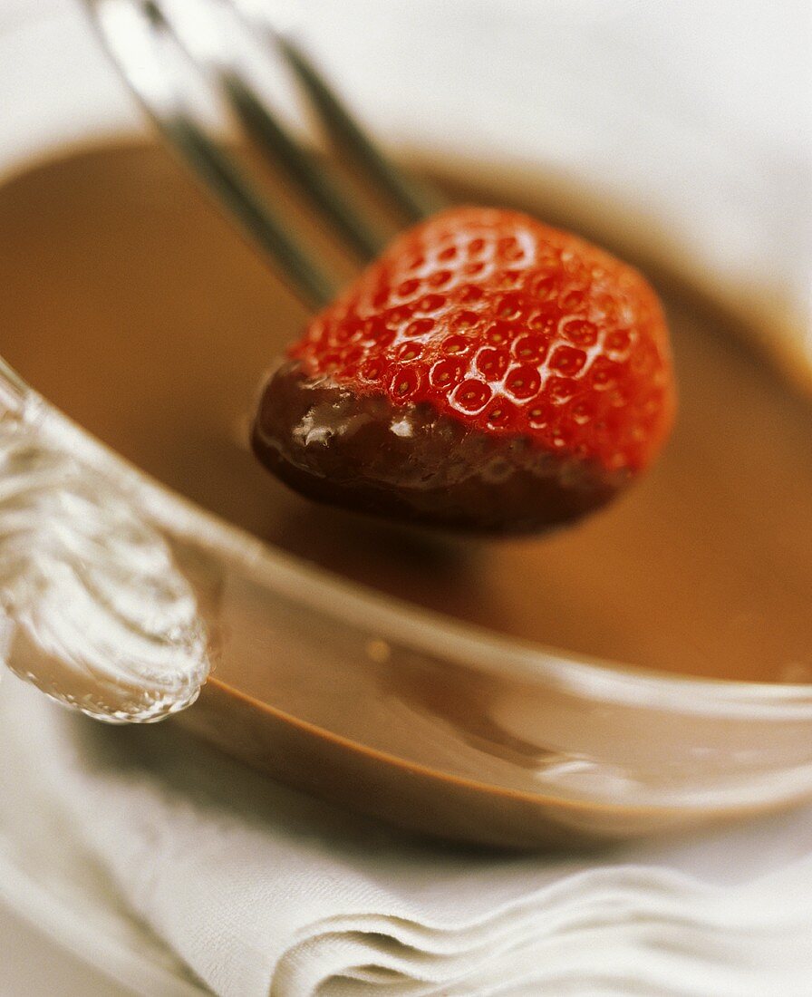 Erdbeere auf Gabel wird in Schokolade getaucht