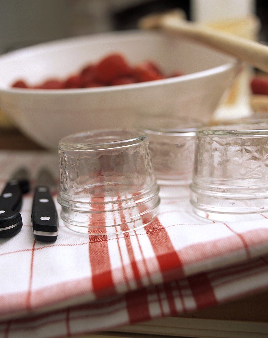 Leere Einmachgläser, dahinter Schüssel mit Erdbeeren