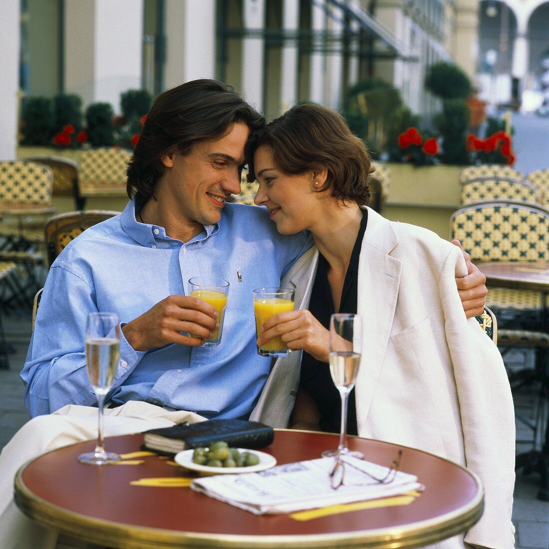 Young couple at café table with orange juice, champagne, olives