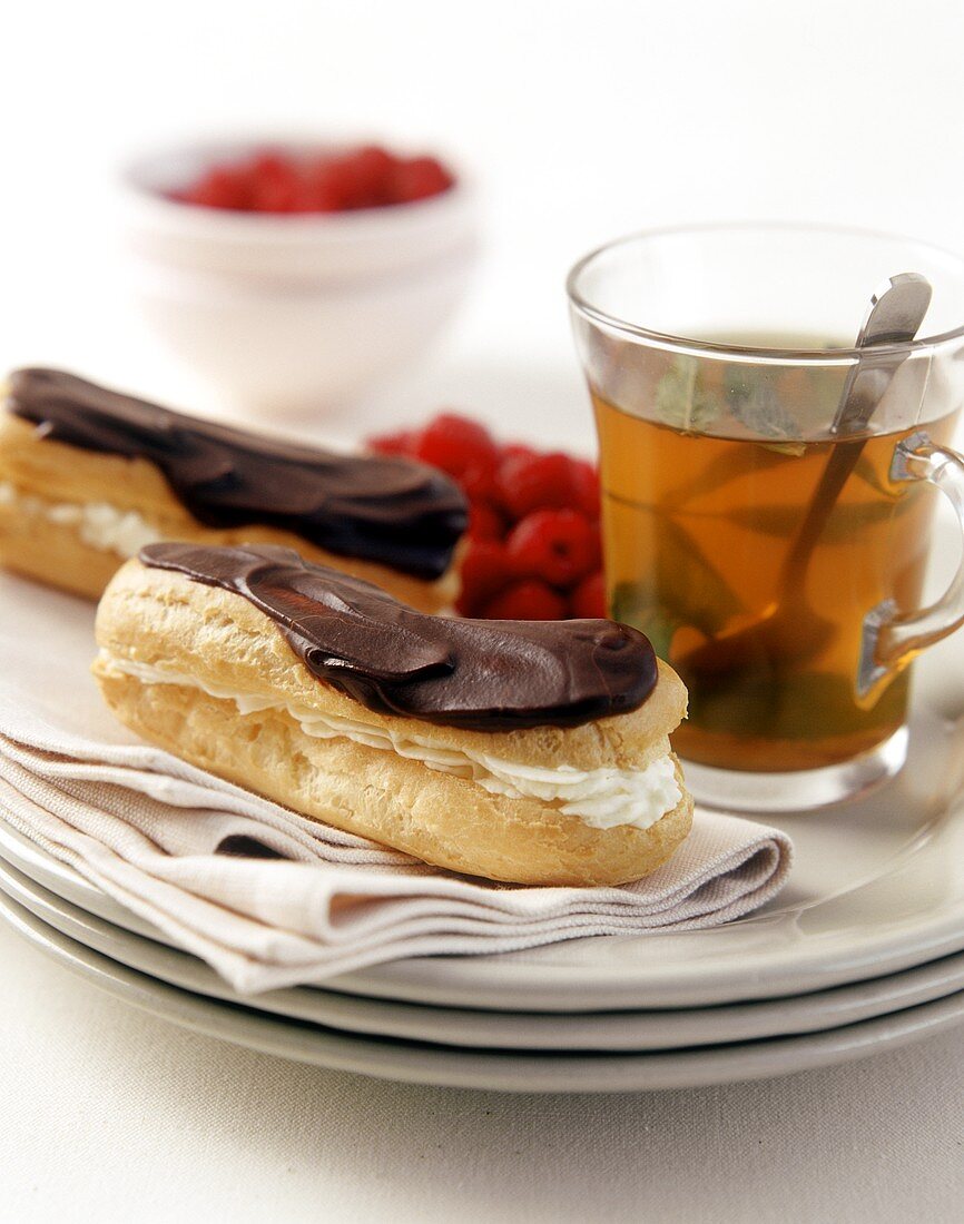 Zwei Eclairs, ein Glas Pfefferminztee, dahinter Himbeeren