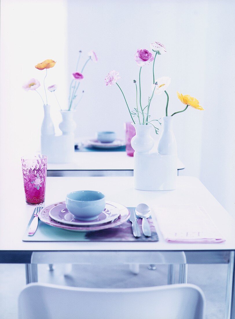 Gedeck in zarten Pastellfarben und Vasen mit Blüten auf Tisch