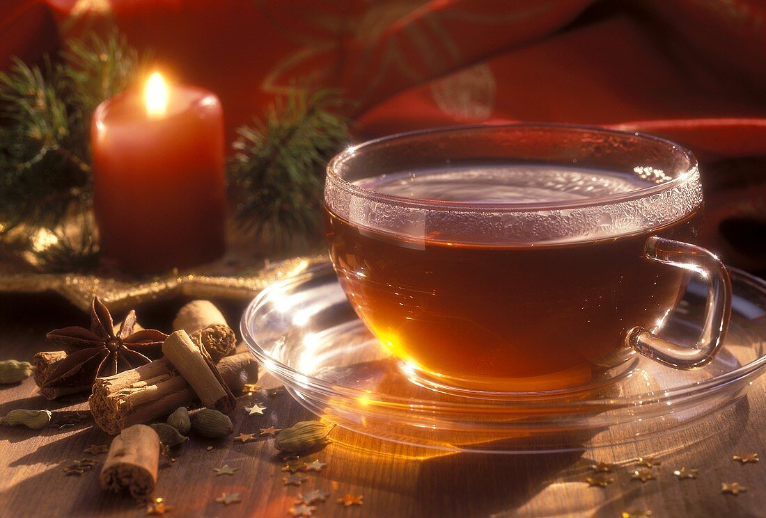 Spiced Christmas tea in glass cup; spices; candle