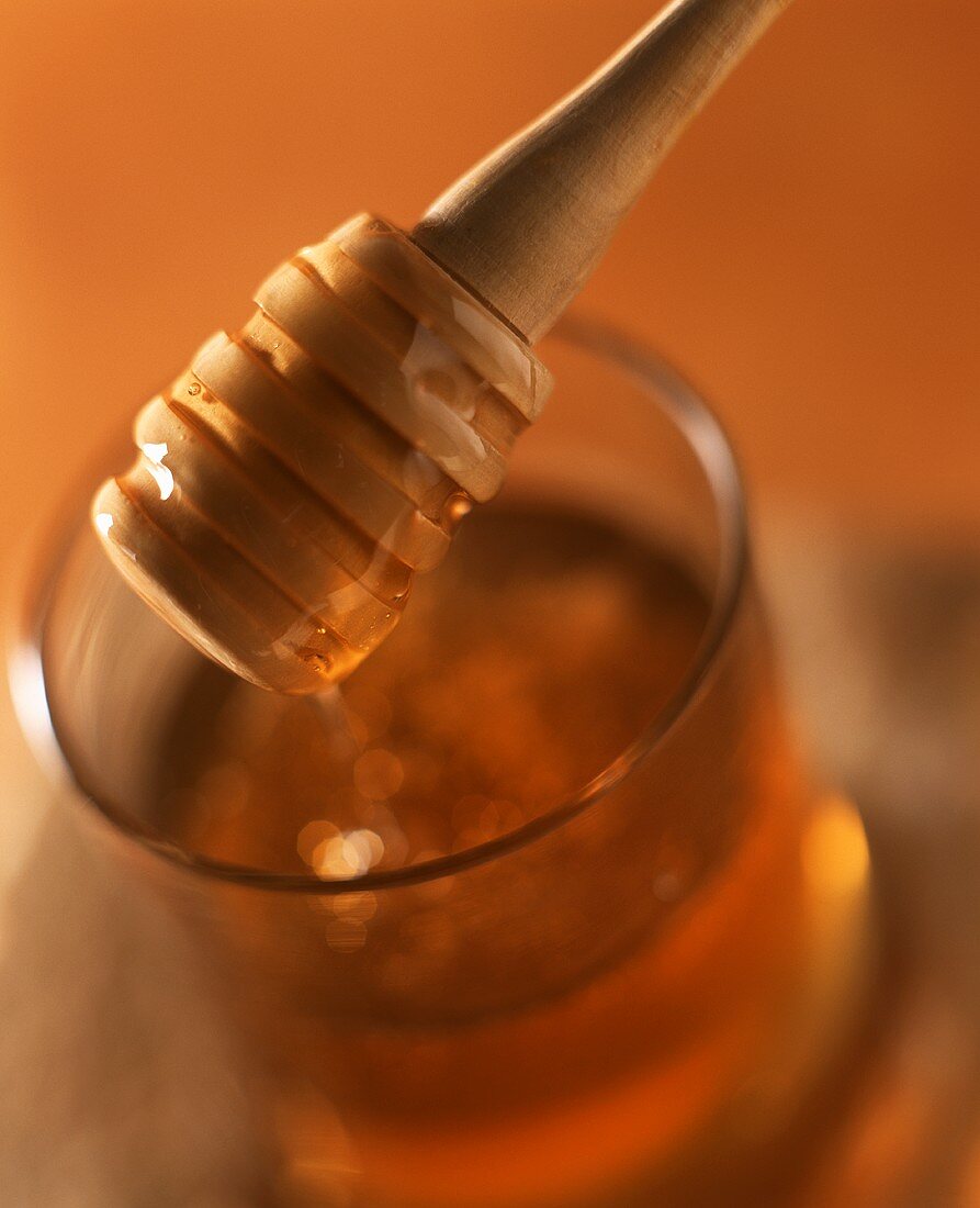 Honig fliesst vom Honiglöffel in ein Glas