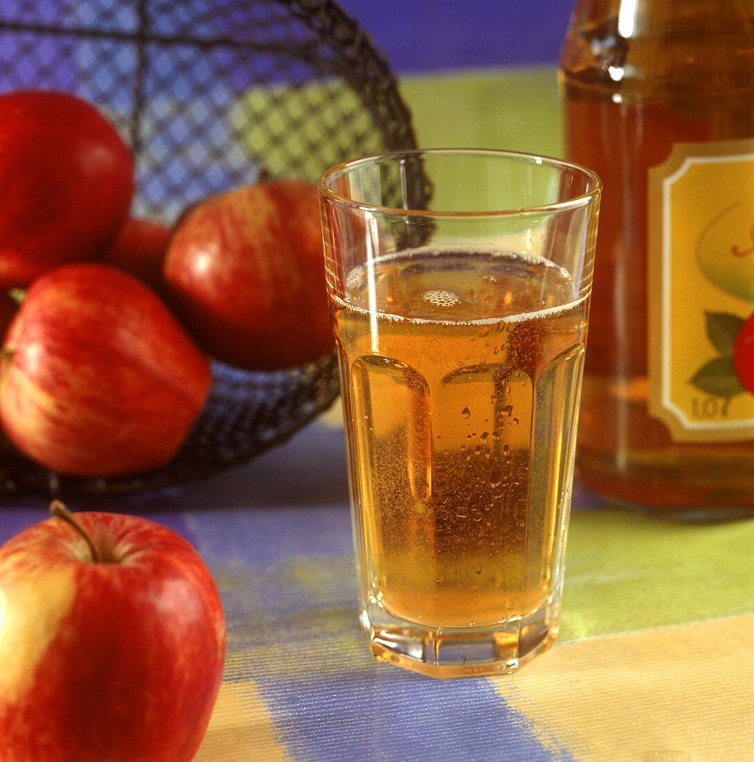 Ein Glas Apfelschorle, daneben Flasche und frische Äpfel