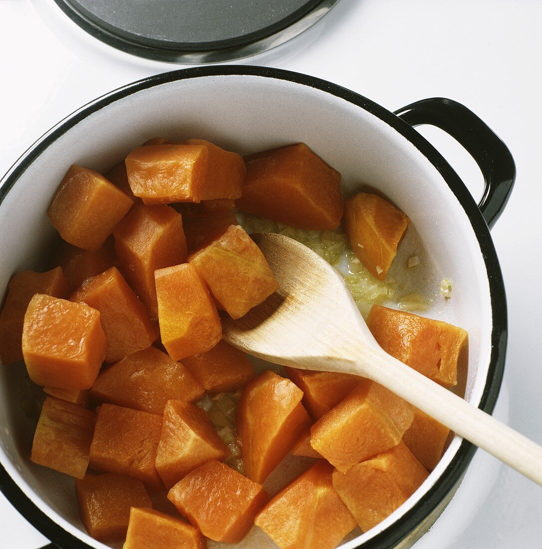 Browning pieces of pumpkin in a pan