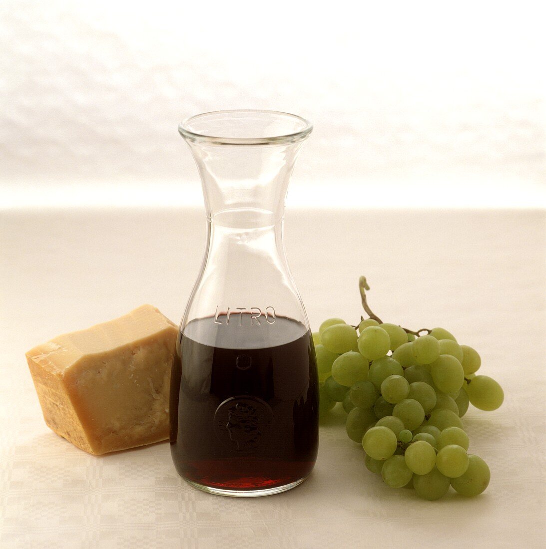 Weinkaraffe mit Rotwein, daneben Parmesan und grüne Trauben