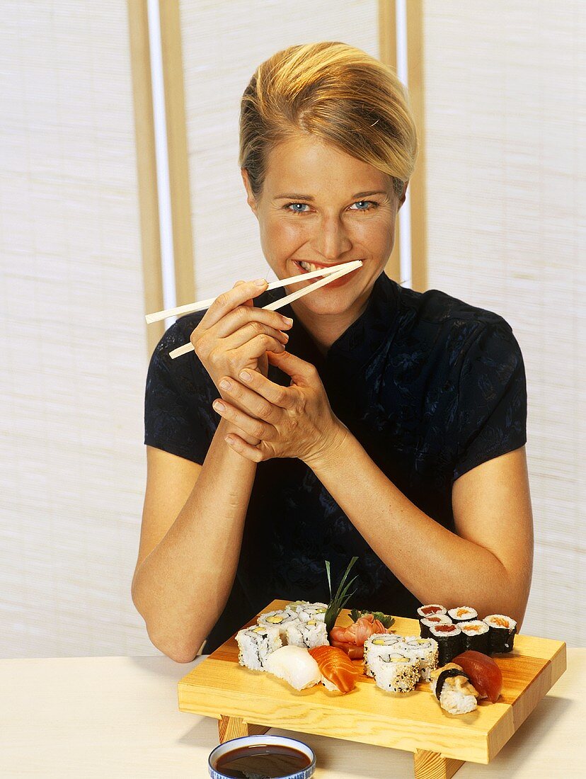 Fröhliche blonde Frau isst Sushi mit Stäbchen