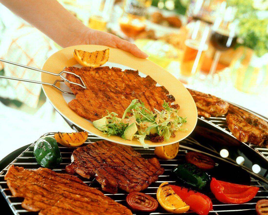 Gegrillte Schnitzel mit Grillzange auf Teller legen