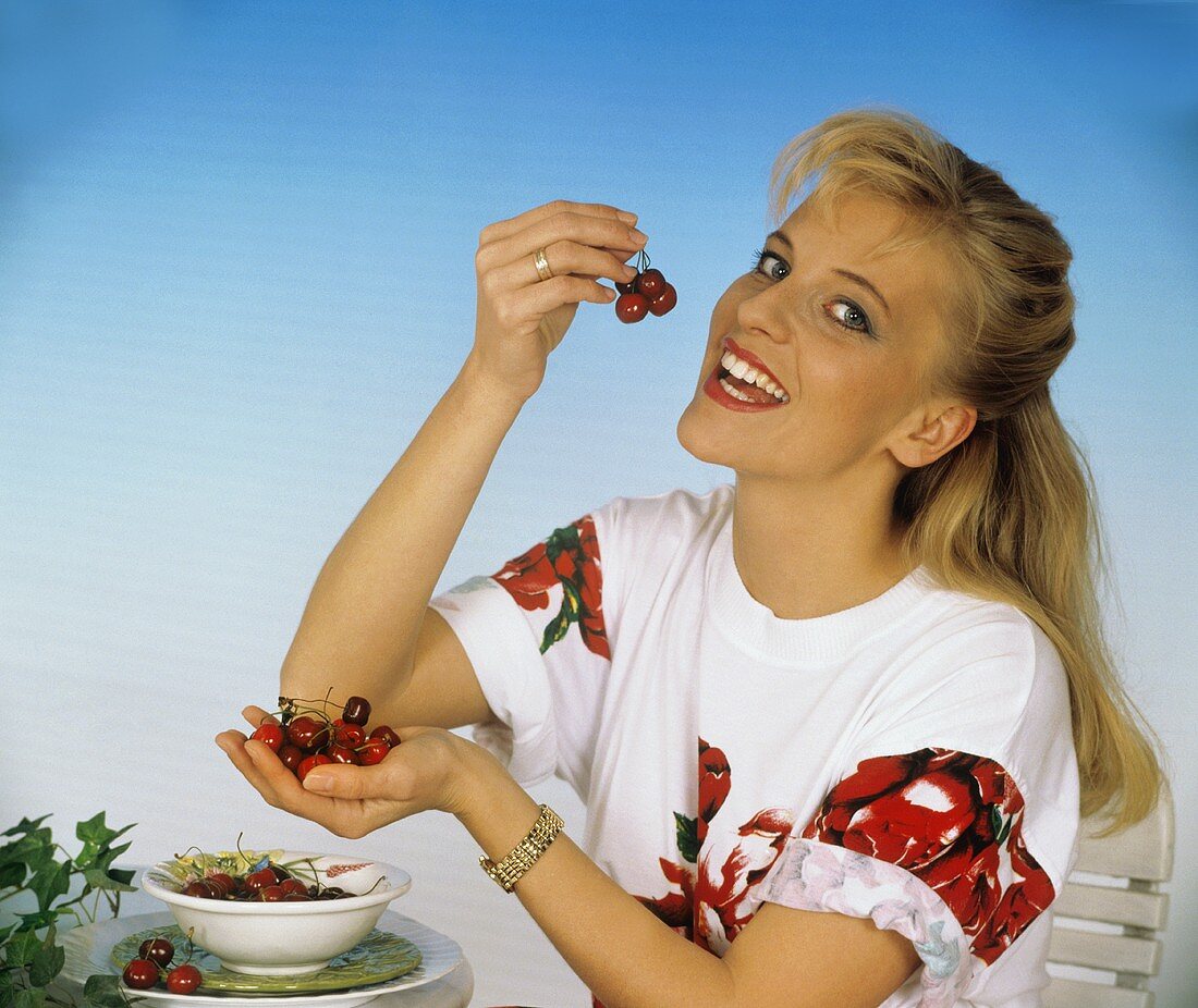Woman biting into a cherry & holding cherries in her hand