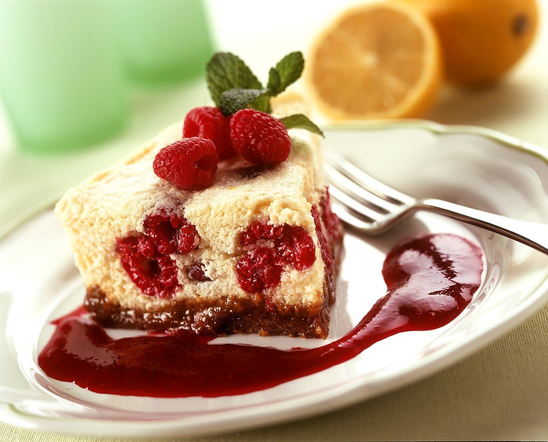 A piece of raspberry quark cake with raspberry sauce on plate