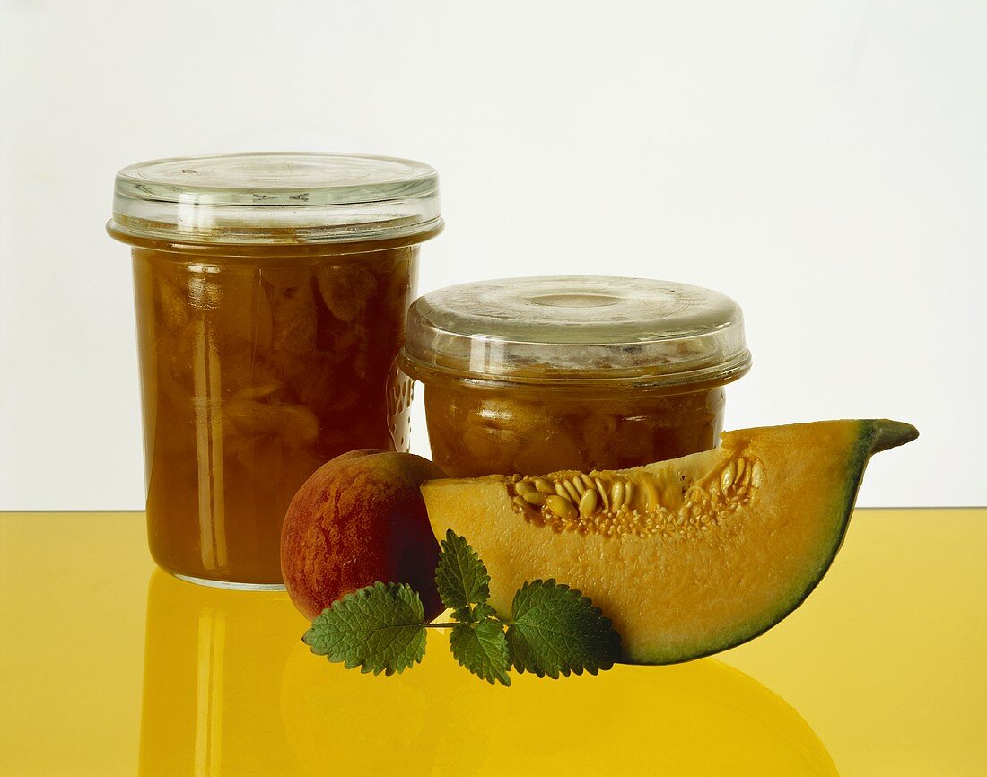 Pfirsich-Melonen-Konfitüre in Gläsern, davor Obst