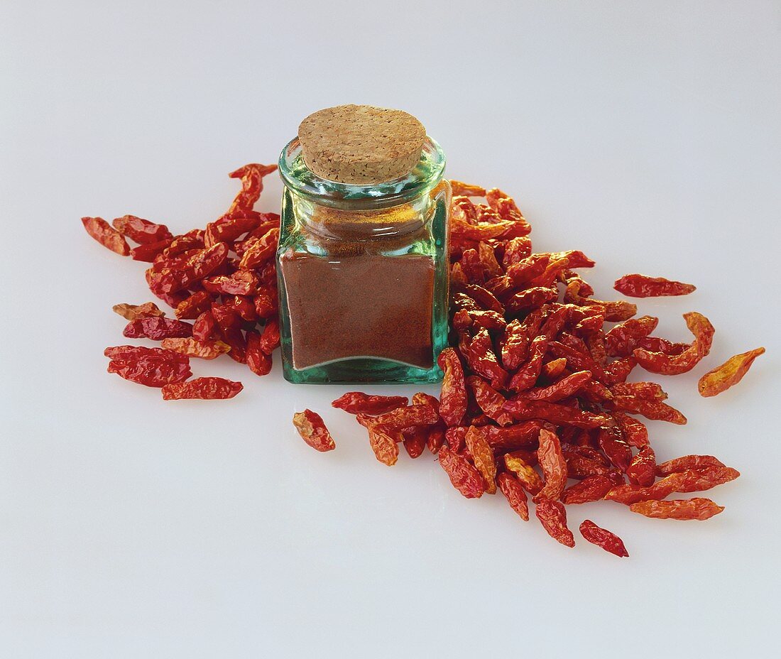 Chili powder in jar, dried chili peppers beside it 