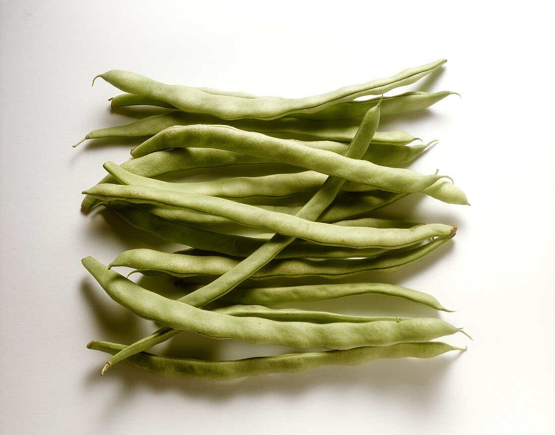 Several green runner beans against white background