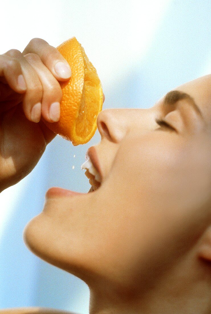 Junge Frau drückt Saft aus einer Orange in ihren Mund