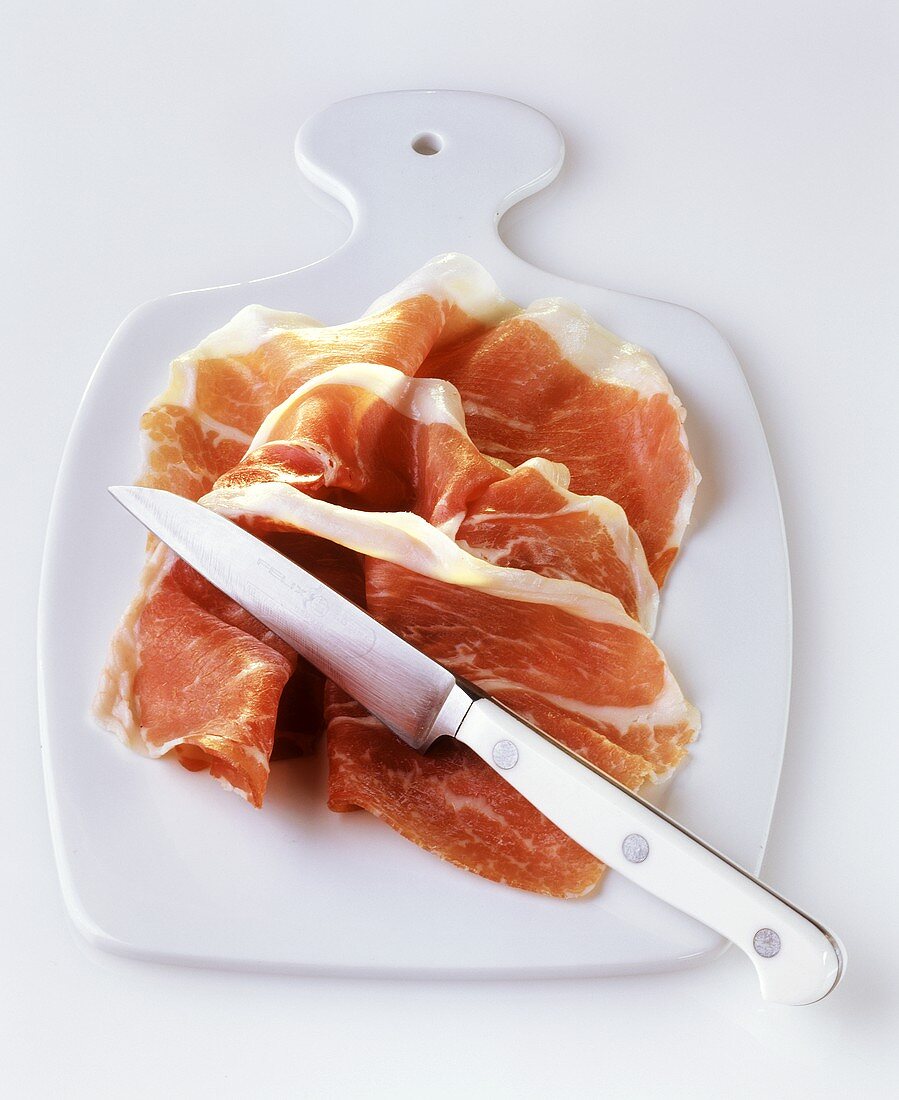 Three slices of ham on chopping board with knife