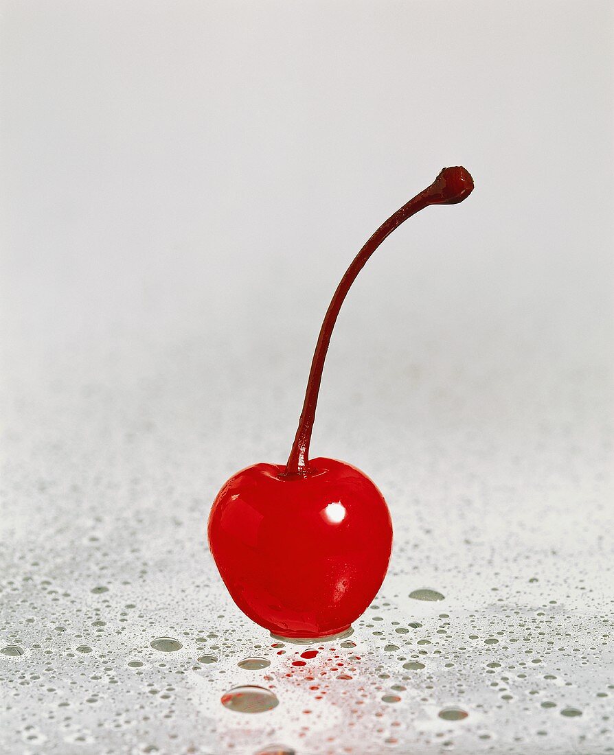 A cocktail cherry on sheet of glass with drops of water