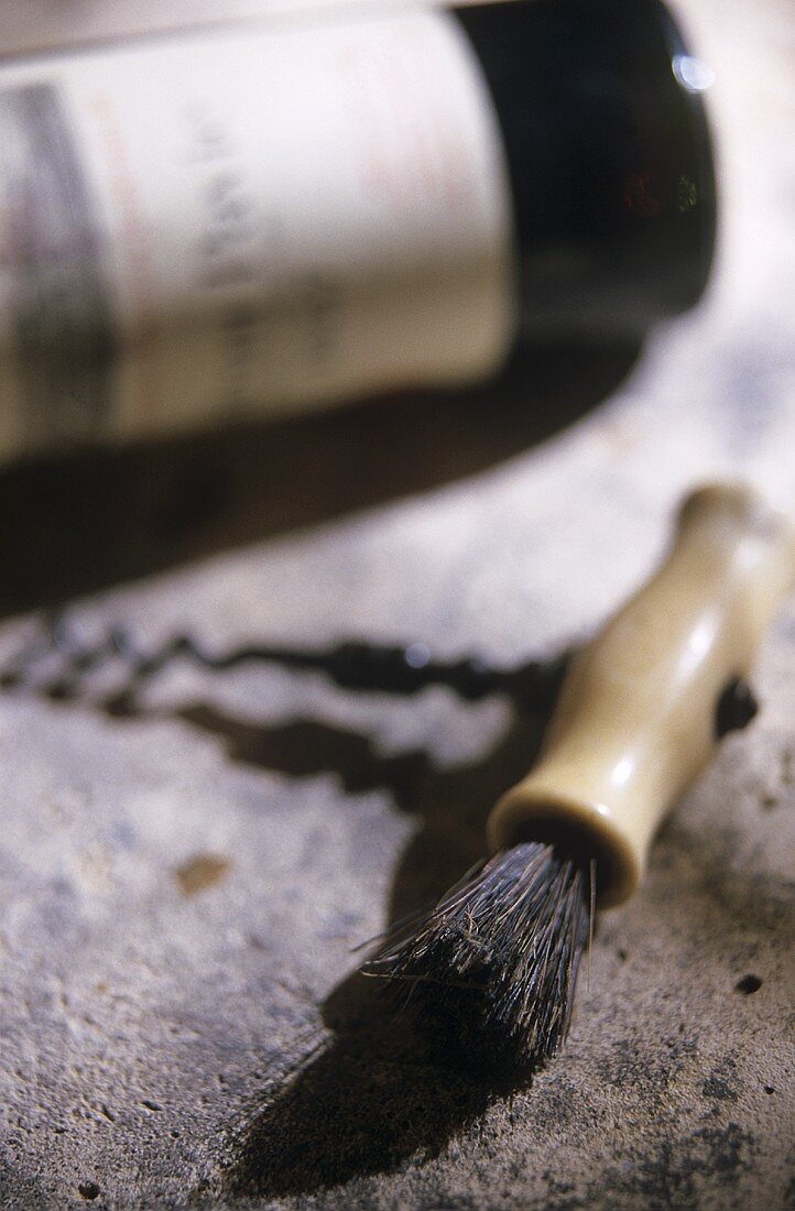 A corkscrew on stone surface in front of red wine bottle
