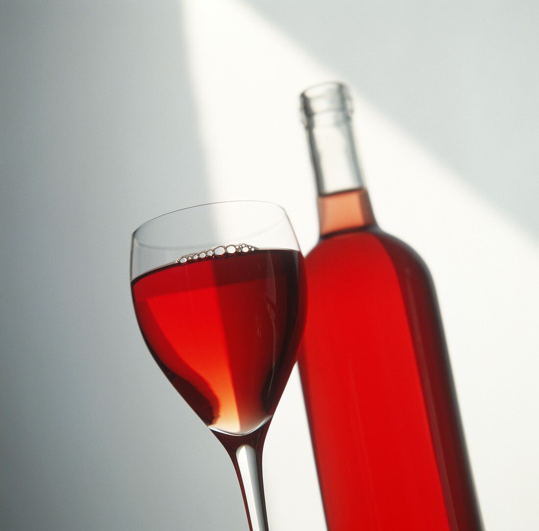 Gefülltes Rotweinglas vor Rotweinflasche