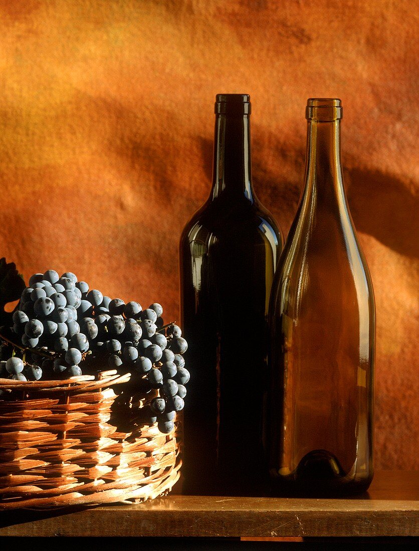 Still life with empty wine bottles & grapes in basket