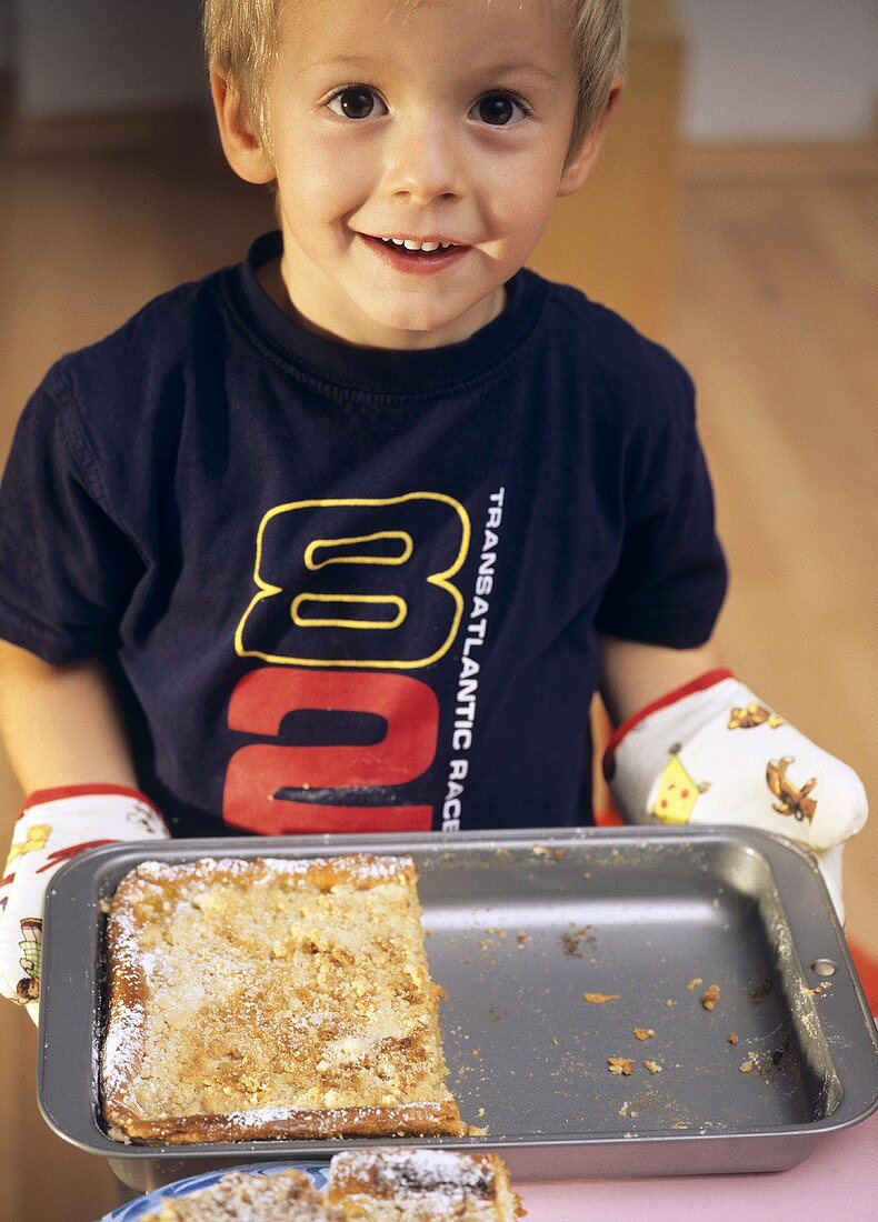 Small boy holding a baking tin with apple cake