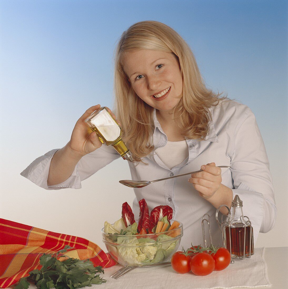 Junge Frau würzt gemischten Salat mit Öl